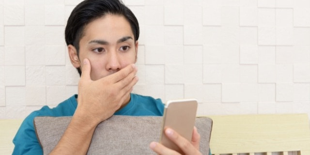 スマホを見ながら口を押さえて驚く男性